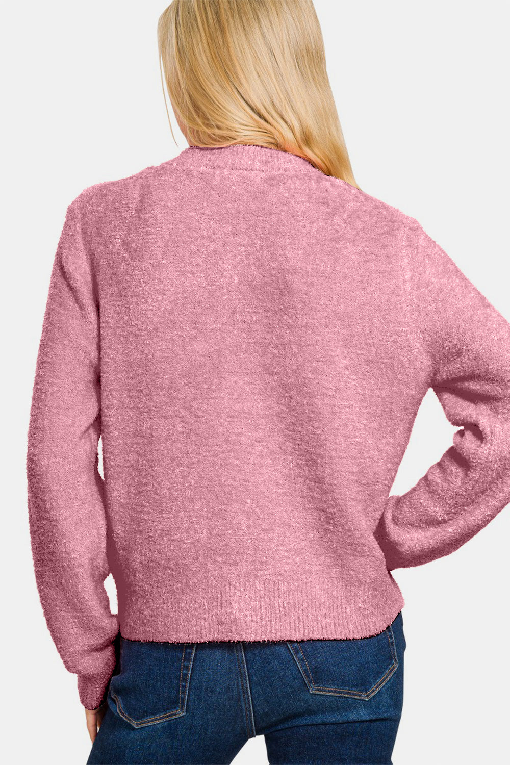 A person with long blonde hair stands with their back to the camera, wearing a Zenana Button Down Long Sleeve Sweater Cardigan in pink and blue jeans. The background is a plain light gray.