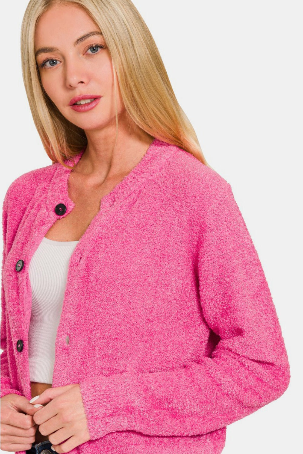 A woman with long blonde hair is wearing a bright pink Zenana Button Down Long Sleeve Sweater Cardigan over a white top. She is looking towards the camera with a neutral expression against a plain white background.