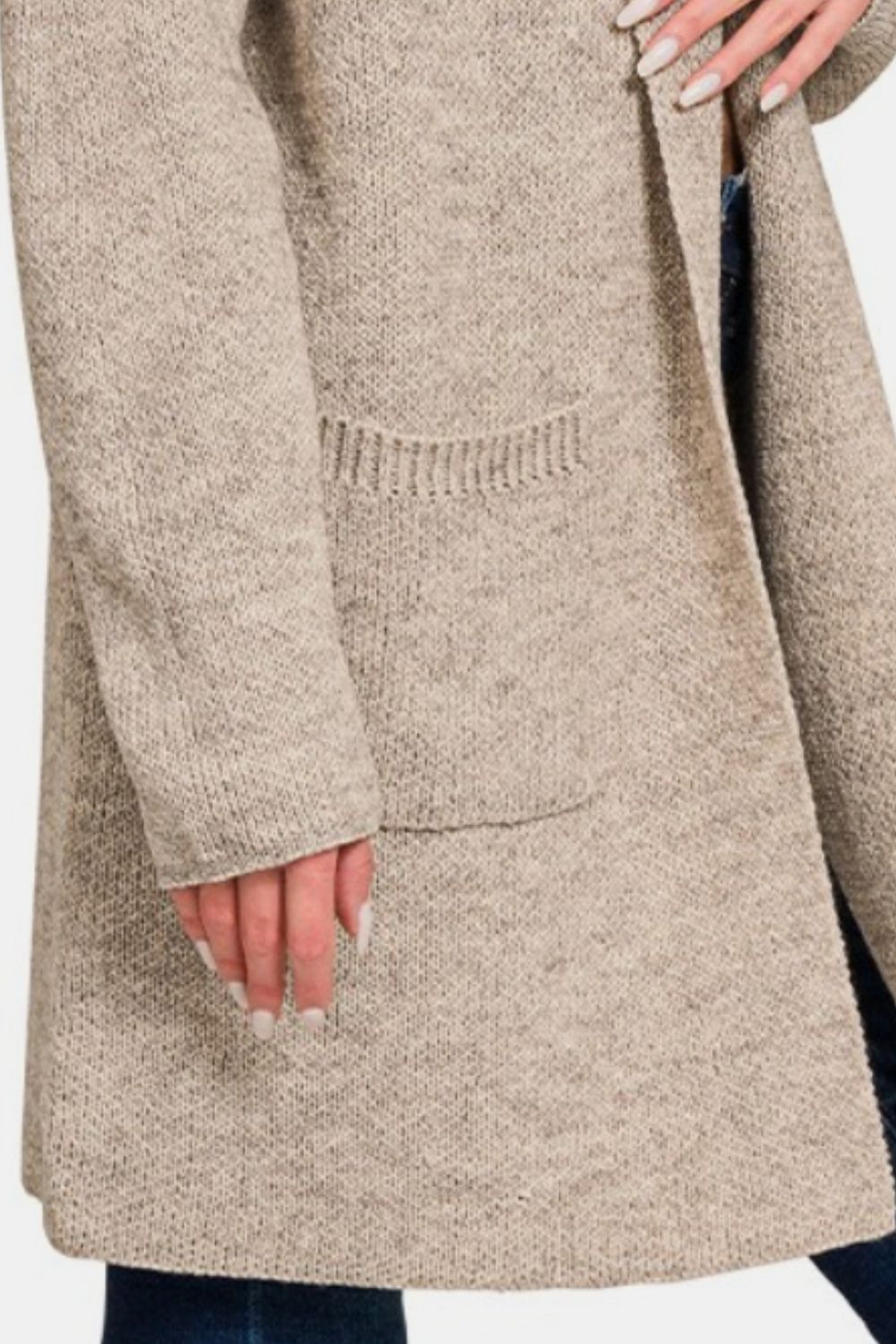 A person wearing the Zenana Hooded Open Front Sweater Cardigan in beige, featuring visible pockets, is paired with dark jeans. The cardigan serves as a perfect layering piece, while their hand rests near the pocket and their nails are neatly manicured.