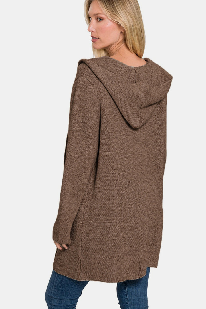 A person wearing the Zenana Hooded Open Front Sweater Cardigan in brown stands sideways, looking back. They have long blonde hair and are paired with blue jeans. The plain white background highlights it as an ideal layering piece for any outfit.