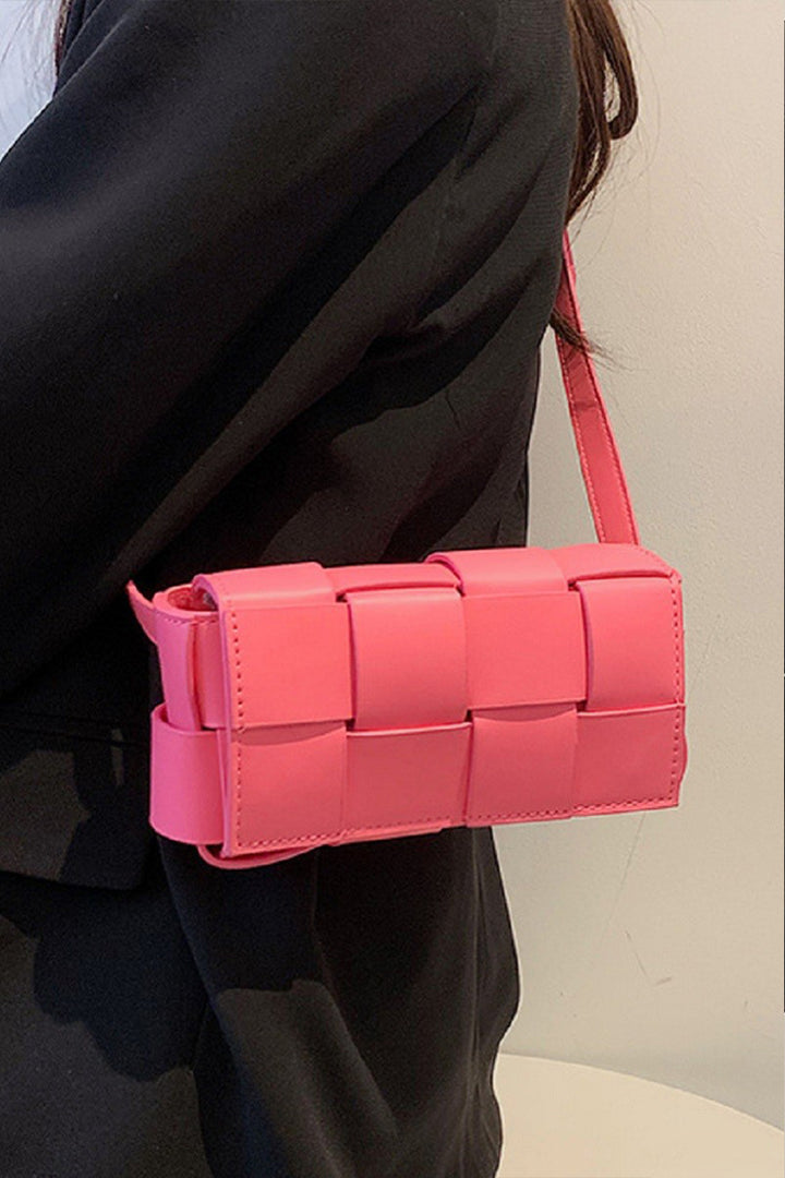 A person in a black jacket carries the Zenana Vegan Leather Woven Crossbody Bag, a small pink rectangular handbag with an eco-friendly strap that blends style and sustainability effortlessly.