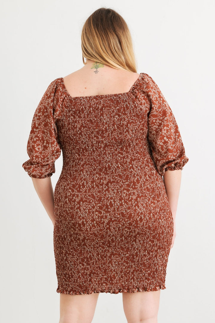 A woman with long hair facing away showcases the Zenobia Plus Size Smocked Printed Square Neck Mini Dress, which is adorned with a colorful print. The dress features puffed sleeves and a square neckline, perfectly complementing the small tattoo visible on her upper back against a plain background.